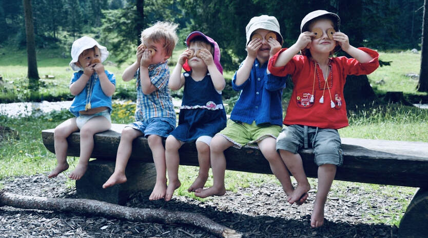 Fünf kleine Kinder auf einer Bank halten sich Willisauer-Ringli vor die Augen